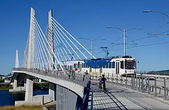 The Tilikum Crossing bridge with a MAX train traveling northbound and pedestrians walking alongside