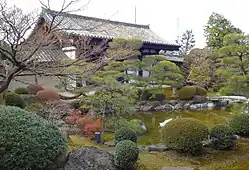Wooden gate with gabled roof and white walls beyond a pond.