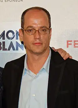 Tom Kalinwearing glasses and a vest outside a light blue shirt, looking to the front