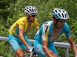 Two riders riding in a line, with one wearing a yellow jersey