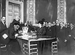 Arroyo drops her ballot into the ballot box. Several people, all men, are waiting in line behind her.