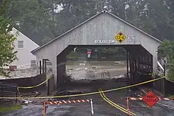 Flood waters on the Ottauquechee River in Quechee scouring the approach to the covered bridge, opposite side.