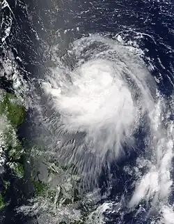 Image of a tropical cyclone to the right of a group of small landmasses. The tropical cyclone is characterized by a sprawling mass of spiralingclouds, though no eye is evident.