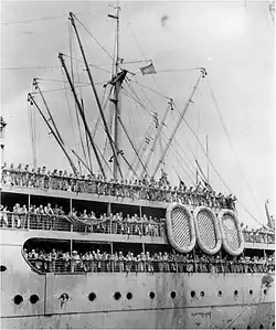 A black and white photograph of a troop transport ship, with soldiers crowding all of its 3 decks