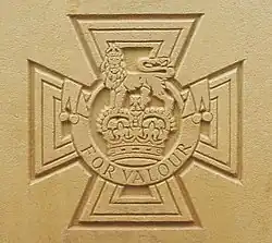 The cross pattée bearing the crown of Saint Edward surmounted by a lion with the inscription FOR VALOUR etched into stone.