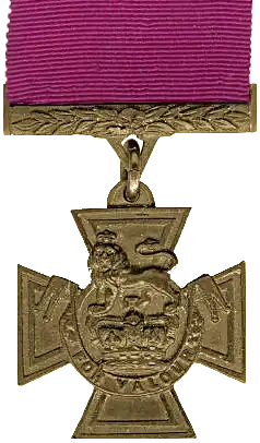 A medal in the shape of a cross hanging from a crimson red ribbon.