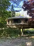 View of part of the structure of the Mushroom House in Perinton, New York, a white, domed structure, from a gravel path with trees in the background and foreground.