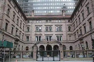 The Villard Houses as seen from across Madison Avenue. There is a black fence in front of the residences, as well as a courtyard immediately behind this fence. At the rear is the hotel tower, which has a black facade and horizontal windows.