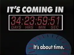 A television screenshot. On a black screen, from top: 1. The words IT'S COMING IN in a bold, white sans serif. 2. Inside a white box, a countdown showing days, hours, minutes and seconds. 3. In the lower right, a blue 3D circle with red elements suggesting the dial faces on a clock and, on top in white, the words "It's about time."