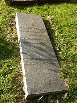 A horizontal gravestone of polished granite, partially sunk on one side