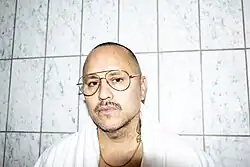 Willy Chavarria, an American fashion designer, standing against a background of plain tiles