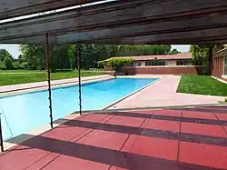 The swimming pool outside the building. The pool deck is made of stone, except in the foreground of image, where the deck is made of red tile.
