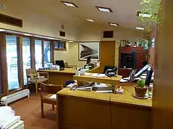 One of the building's offices. There is a desk in the foreground and windows to the left. The ceiling slopes down slightly from left to right.
