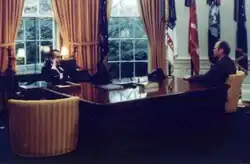 Nixon seated behind the Wilson desk and Ford seated next to it.