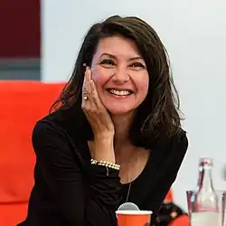 Uśmiechająca się siedząca kobieta z włosami do ramion widziana do pasa opiera swoją prawą dłoń o prawy policzek