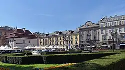 Plac widziany ze wschodu. Od lewej Dom pod Krzyżem, przed nim dawny parking a wcześniej dworzec autobusowy obecnie (rok 2020) po rewitalizacji, dalej Hotel Pollera, Dom Pollerów, Kamienica Murdzieńskich. Na pierwszym planie skwer im. Jacka Woźniakowskiego.