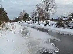 Drewniane domy pokryte śniegiem w pobliżu cieku wodneg częściowo skutego lodem