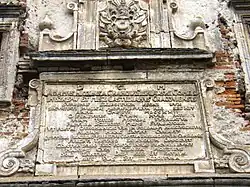 Tablica pamiątkowa z herbem szlacheckim Leliwa na bramie miejskiej, na niej łacińska inskrypcja upamiętniająca Adama Mikołaja Sieniawskiego