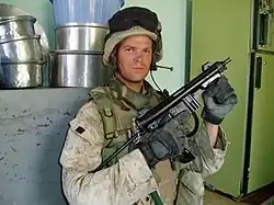 Żołnierz pozujący do zdjęcia w mieszkaniu, trzymający Berettę M12S.