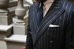 &nbsp;Biała poszetka w brustaszy, złożona techniką TV-fold, w garniturze w prążek.