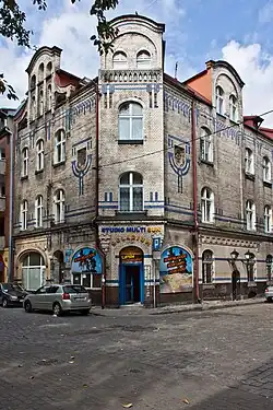 Fotografia barwna, kamienica narożna o fasadzie pokrytej glazurowaną cegłą w kolorach białym i granatowym