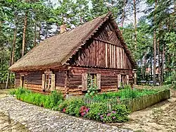 Zabytkowa, drewniana chałupa, wokół rosną kwiaty, w tle las