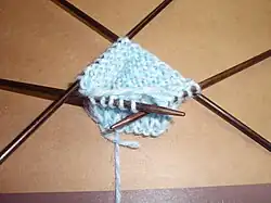 Zdjęcie robótki na drutach. W kadrze widać wydziergany fragment zaczepiony na czterech drewnianych drutach.