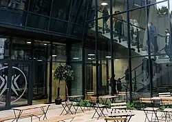 widać dziedziniec z krzesełkami, za nim oszklony budynek z logo Polskiego Teatru Tańca, w budynku na schodach grupka widzów