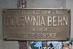 Metalowa tablica z nazwą producenta kolei, w budynku dolnej stacji