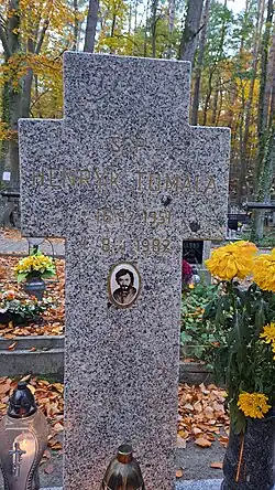 Kamienny nagrobek w kształcie krzyża z wyrytymi, pomalowanymi na złoto literami – napis: „Ś.P. Henryk Tomala, 16 12 1951 – 8 1 1982”. Pod napisem zdjęcie Tomali na tzw. porcelance. Przy nagrobku stoją znicze oraz żółte chryzantemy. Jesień.