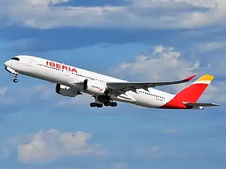 Zdjęcie samolotu w locie. Duży pasażerski z uniesionymi końcówkami skrzydeł. Biały samolot z czerwonymi i złotymi akcentami.