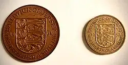 Fotografia przedstawia dwie monety z Jersey z czasów przed decymalizacją. Po lewej stronie zdjęcia znajduje się moneta o nominale 1/12 szylinga. Na jej rewersie, widocznym na zdjęciu znajduje się herb Jersey - trzy lwy oraz napis informujący o emitencie, dacie wybicia i nominale (Bailiwick of Jersey, 19-64, One twelfth of a shilling). Po prawej stronie zdjęcia znajduje się mosiężna moneta o nominale 1/4 szylinga. Na jej rewersie, widocznym na zdjęciu, podobnie jak przy monecie 1/12 szylingowej,  znajduje się herb Jersey - trzy lwy oraz napis informujący o emitencie, dacie wybicia i nominale (Bailiwick of Jersey, 19-57, One fourth of a shilling