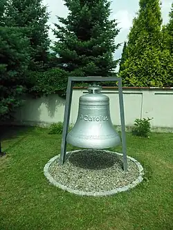Srebrny dzwon średnicy ok. jednego metra zawieszony w ogrodzie kościelnym, na nim napis S. Carolus