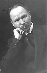 Czarno-białe zdjęcie portretowe mężczyzny w średnim wieku. Mężczyzna ma opiera brodę o rękę.