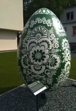 w środku obrazu pomnik jajka wielkanocnego (kroszonki) w kolorze zielonym ozdobionym białym wzorem w motywy kwietne