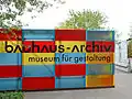 Podłużna plansza przy budynku muzeum będąca zestawem prostokątnych pól w kolorach: czerwonym, żółtym i niebieskim, z naniesionym na nich napisem: bauhaus-archiv, museum für gestaltung
