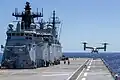Zaparkowany śmigłowiec oraz lądujący samolot Bell-Boeing V-22 Osprey na pokładzie HMAS Canberra