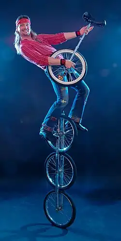 Mężczyzna na monocyklu trójkołowym trzymający zwykły monocykl niczym gitarę