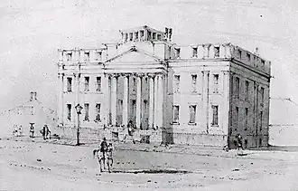 Black and white drawing of a large three-storey building fronted by a four-column portico. A man on a light-coloured horse is riding down the wide empty street in front of the building