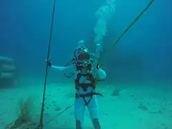 Ćwiczenia przed NEEMO 18. Pesquet pod wodą, w kombinezonie nurka, stoi na morskim dnie i pozuje do zdjęcia.