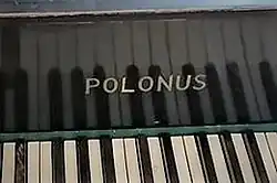 Napis POLONUS nad klawiszami fortepianu