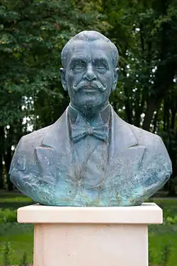 Zdjęcie przedstawia popiersie Ignacego Mościckiego na betonowym cokole. Mościcki ubrany jest w garnitur, koszulę i muszkę. Na jego twarzy znajdują się podkręcane na końcach wąsy, a na górze głowy ma włosy, które pozostawiają zakola.