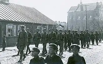 Przemarsz kompanii POW pod dow. Stanisława Zdanowskiego przez Łuków; 1918 r. lub wcześniej, w tle kościół Podwyższenia Krzyża Świętego