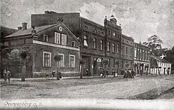 Na czarno-białej pocztówce z podpisem Georgenberg O. S. Rathaus widać szereg pięciu budynków, przed którymi przebiega droga, wzdłuż której rosną niewielkie drzewka oraz przechadzają się elegancko ubrani ludzie