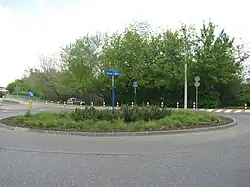 Zdjęcie. Nieduże rondo pośrodku którego umieszczono okrągły klomb pośrodku którego umieszczono tablicę z nazwą ronda.