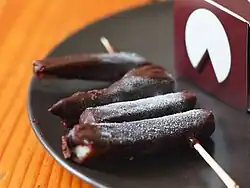 Na talerzu znajdują się cztery sztuki słoninyw czekoladzie nabite na drewniany patyczek