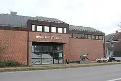 Zdjęcie. Duży budynek z cegły z dużym przeszklonym wejściem. Przed budynkiem rzeźba niedźwiedzia.