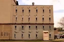 Mural na zachodniej ścianie kamienicy przedstawiający dziewczynę z karabinem autorstwa Hyuro﻿(inne języki) (2012)