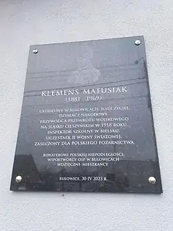 Mieszcząca się na ścianie budynku czarna tablica z wizerunkiem Klemensa Matusiaka oraz jego krótkim biogramem.