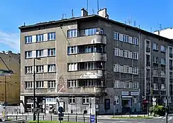 Ul. Pawia 12 na rogu z ul. Worcella.Kamienica proj. Jakub Jan Spira (1937). Na fasadzie godło kamienicy „Pastuszek z pawiem”